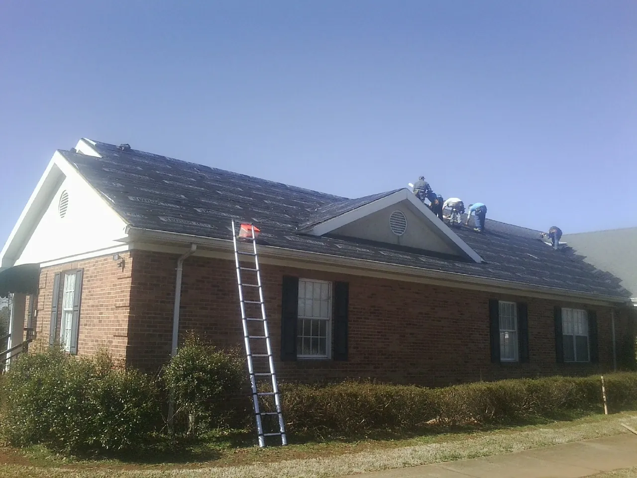 Crew tearing shingles off a brick ranch roof with a ladder set — Metal Roof Repair work by our crew in Dillon